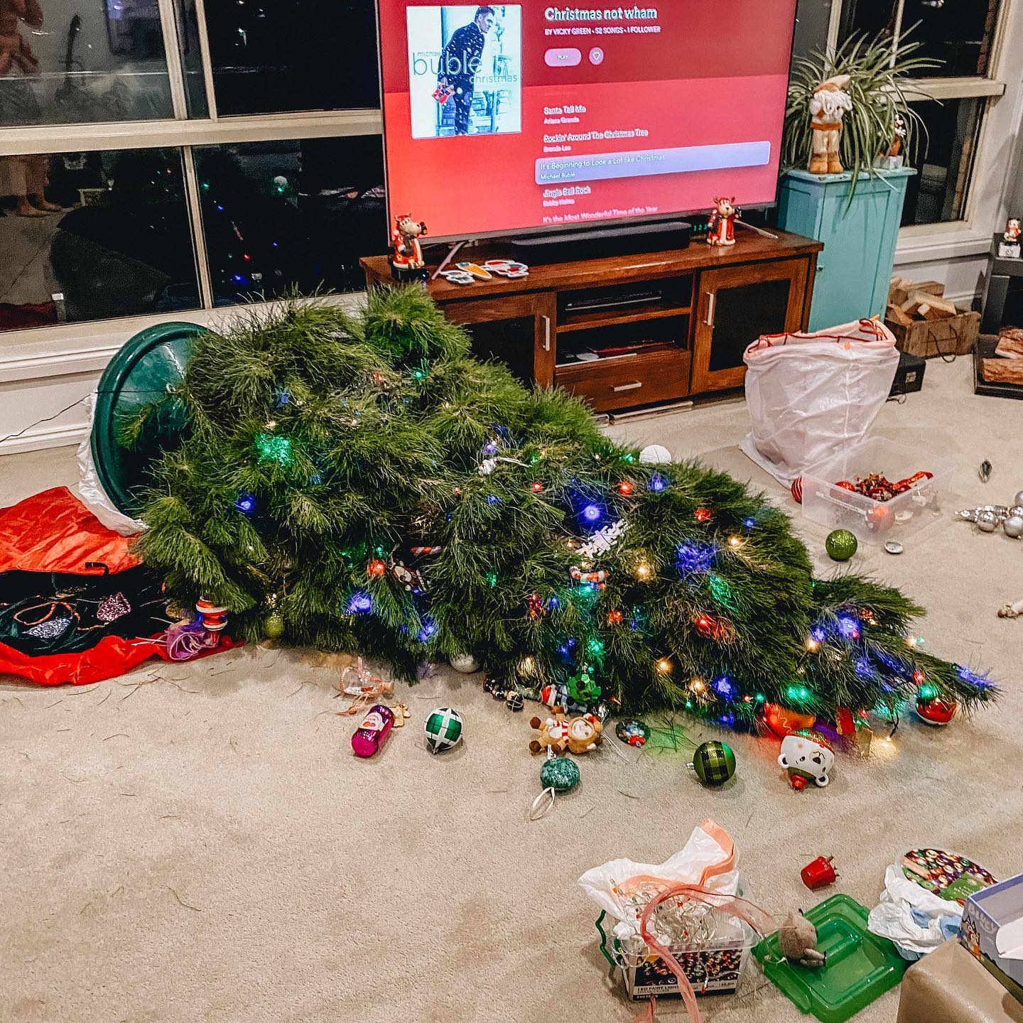 A fallen christmas trees laying on the carpet surrounded by fallen baubles