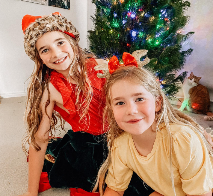 Two kids in front of a Christmas tree with a naughty cat in the background